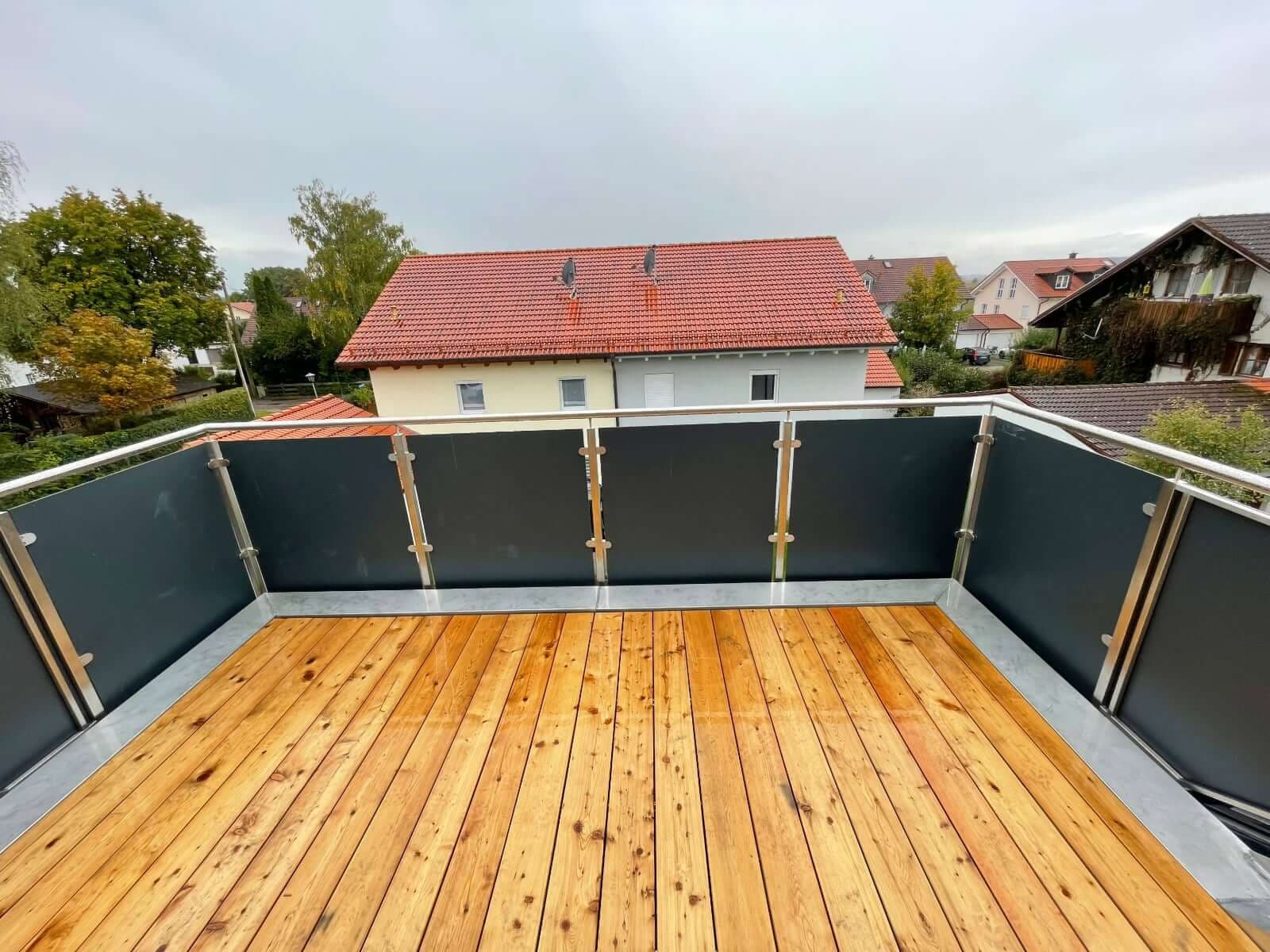 Balkon mit Holzdielen und Metallgeländer mit anthrazitfarbenen Sichtschutzfeldern