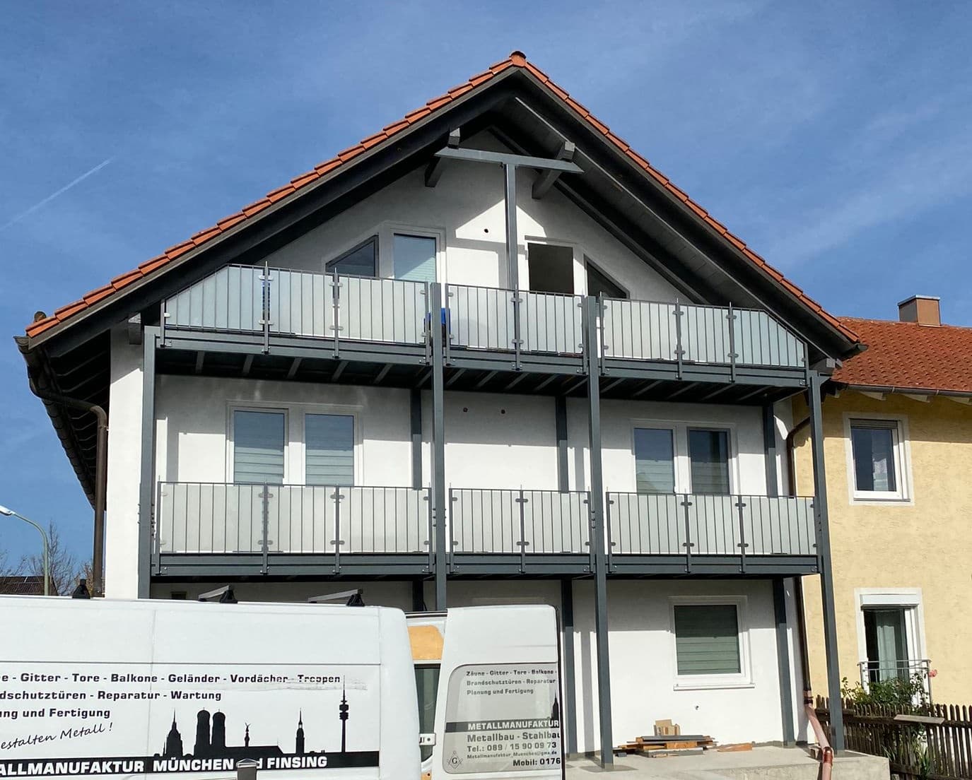 Zweigeschossige Balkonanlage aus dunkelgrauem Metall mit Geländer und Sichtschutzelementen an einem Wohnhaus.